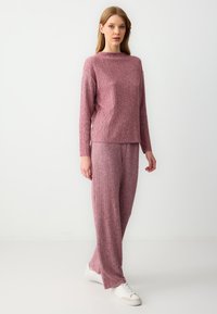 Różowy, dzianinowy komplet odzieży domowej z teksturowanym wzorem; góra z długimi rękawami i okrągłym dekoltem, w połączeniu z luźnymi spodniami.