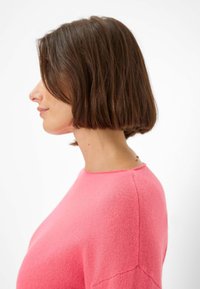 Rosa Strickpullover mit rundem Halsausschnitt und kurzen Ärmeln, der eine weiche Textur und sichtbare Nähdetails aufweist.
