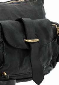 Borsa a tracolla in pelle nera con patta frontale, accentuata da un anello in metallo dorato e superficie testurizzata con cuciture a vista. Chiusura con zip.