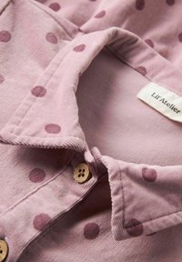Rosa Cordhosenhemd mit lila Pünktchen, ausgestattet mit einem Umlegekragen und Holzknöpfen. Das Etikett trägt die Aufschrift "Lil' Atelier."