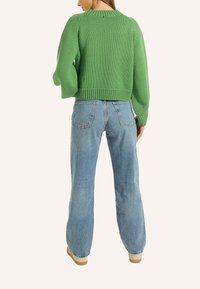 Grüner gestrickter Crop-Pullover mit strukturierter Oberfläche, kombiniert mit hellblauen High-Waist-Jeans und beigen Schnürschuhe.