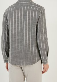 Grijze langshirt met witte verticale strepen, gemaakt van een textuur stof. Voorzien van een kraag en knoopmanchetten. Achteraanzicht wordt weergegeven.