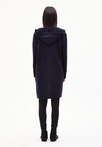 Cardigan long bleu marine en matériau doux avec une capuche, à manches longues et avec des poignets côtelés, longueur genoux et coupe décontractée.