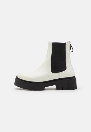 White patent leather Chelsea boots with black elastic side panels and a thick, textured black outsole. Features a pull tab at the back.