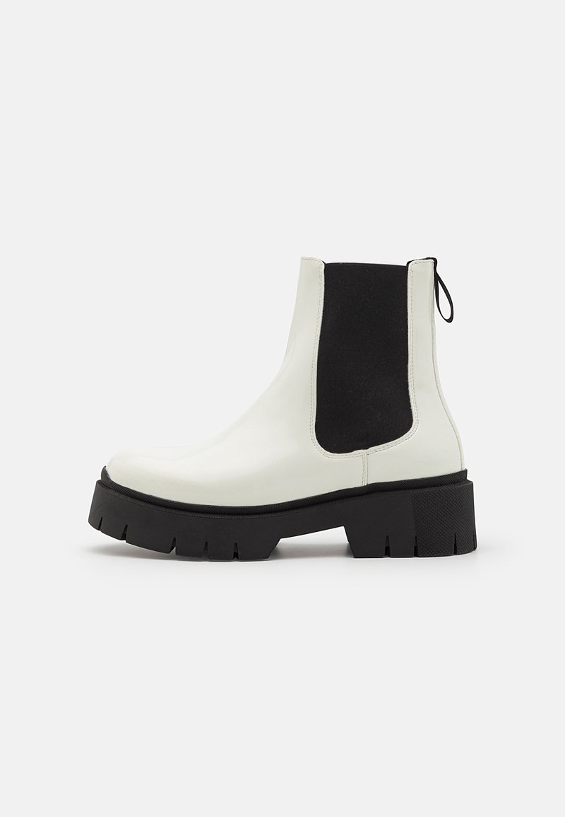 Cizme Chelsea din piele patent albă, cu panouri elastice laterale negre și o talpă groasă, texturată, de culoare neagră. Au un maner de tragere la spate.
