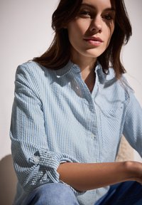 Camicia button-up realizzata in tessuto leggero, con strisce blu e bianche, colletto e maniche arrotolate con dettagli a bottoni.
