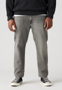 Jeans de denim gris con un corte recto, que presentan un lavado desgastado y detalles de costura sutiles, combinados con zapatillas altas negras.