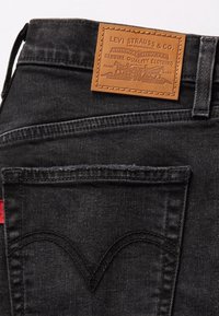 Gros plan de la poche arrière d'un jean en denim noir avec une étiquette en cuir marron Levi Strauss & Co. cousue au-dessus.