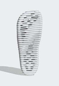 Vit skosula med en vågig, räfflad yta, som har utskärningar och en rundad tå. Materialet verkar flexibelt och lätt.