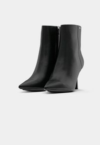 Botines de cuero negro hasta el tobillo con punta afilada y tacón delgado. Presentan un cierre lateral y una textura suave con un diseño minimalista.