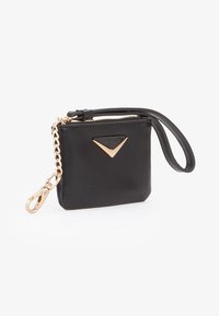 Pochette da polso rettangolare nera con cerniera dorata, targhetta triangolare dorata e catena dorata attaccata con moschettone.