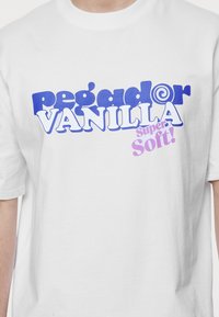 Valge puuvillane t-särk, millel on julge sinine ja lilla kiri, mis ütleb "Pegador Vanilla Super Soft!" mängulises, ümaras fondis.