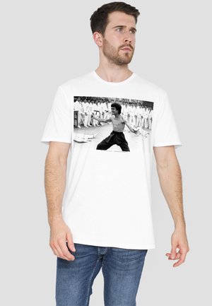 White cotton t-shirt featuring a black-and-white graphic of a martial artist. Short sleeves and relaxed fit with a round neckline.