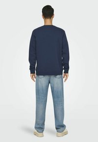 Mørkeblå sweatshirt med lange ærmer, rund hals og ribbet kant, parret med lyseblå vidde jeans og beige sneakers.