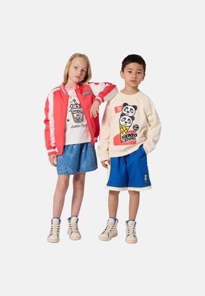 Veste bomber rouge, T-shirt blanc avec motif graphique, jupe en jean bleue sur une fille ; sweat crème avec motif panda, short bleu sur un garçon ; chaussures beiges.