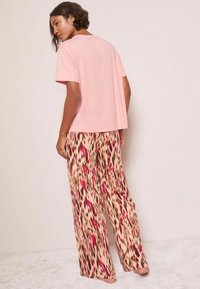 Kerge roosa lühikeste varrukatega ülikond, millele on sobitatud laiad püksid, millel on beež alus ja abstraktne punase ja pruuni loomamustriga kujundus.