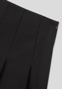 Gonna nera in tessuto con cuciture verticali e zip laterale su uno sfondo grigio chiaro uniforme.