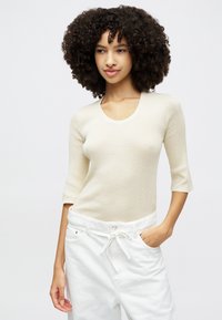 Pull en maille côtelée de couleur beige clair avec un décolleté arrondi et des manches trois-quarts, associé à un pantalon blanc avec cordon de serrage. Texture lisse, coupe décontractée.