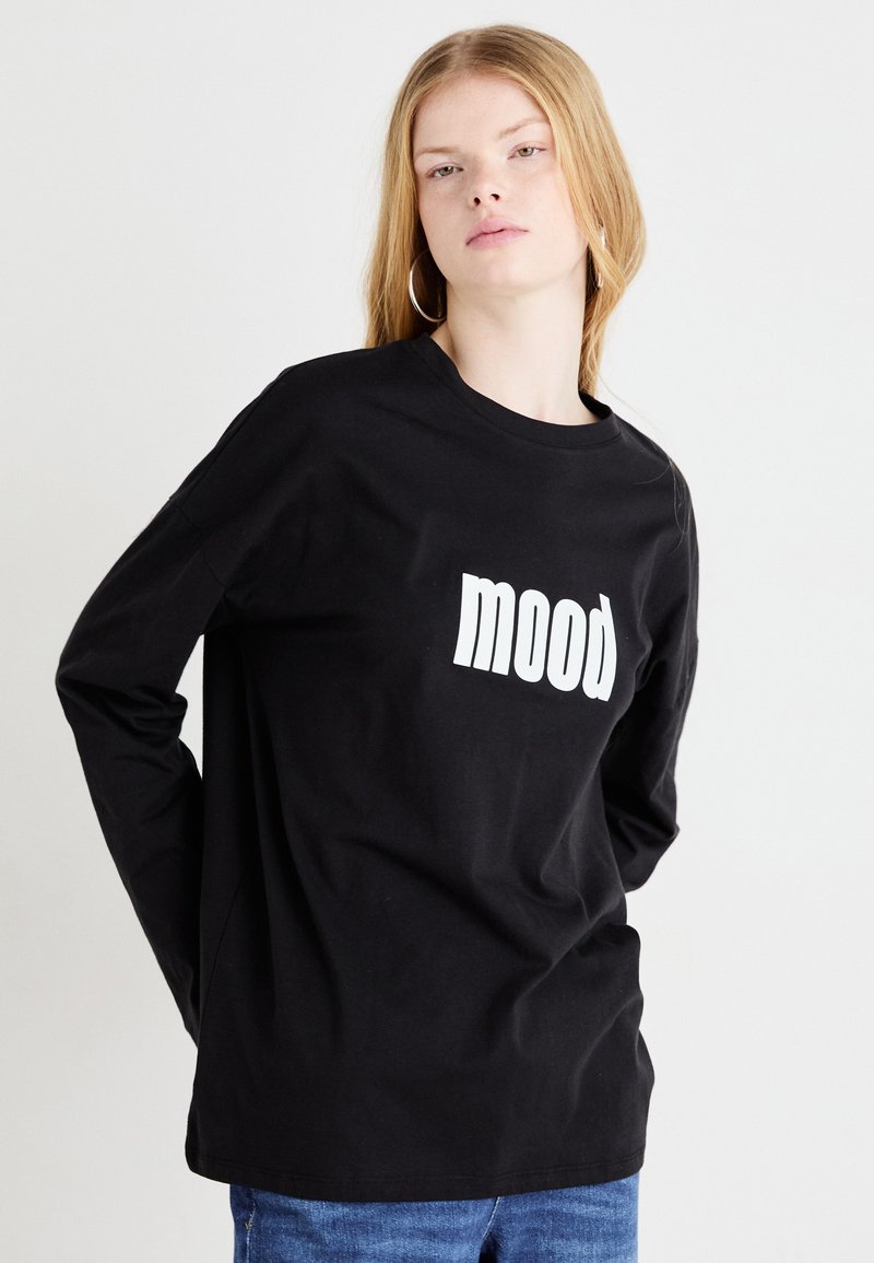Crna majica dugih rukava od pamuka, s bijelim grafičkim natpisom "mood" sprijeda. Jednostavni dizajn s okruglim izrezom.