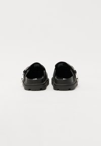 Black sandals with a chunky sole, textured upper, adjustable strap, and silver hardware accents. Smooth inner lining visible.