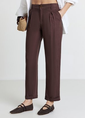 Pantalon marron plissé en tissu lisse, avec une taille haute, des poches latérales et des revers roulés, assorti à des ballerines noires texturées.