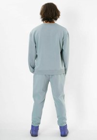 Helles blaues Sweatshirt und passende Jogginghose aus weichem Material. Verfügt über gerippte Bündchen und einen lockeren Schnitt, kombiniert mit blauen Schuhen.