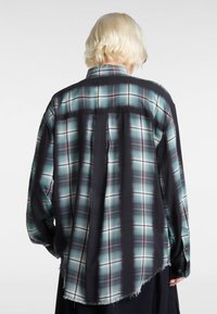 Chemise à carreaux noire et sarcelle avec une texture douce, des manches longues, un ourlet arrondi et des bords effilochés. Dotée d'un col boutonné et de plis au dos.