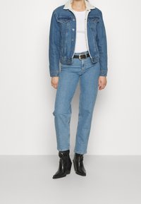 Džínová bunda s beránkovým límcem, přiléhavý silueta. Světle modré džíny, rovného střihu. Černé kožené kotníkové boty s mírným podpatkem.