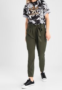 Svartvit blommig t-shirt med leopardmönstrad detalj, olivgröna byxor med hög midja och knytning i midjan, samt svarta sneakers.