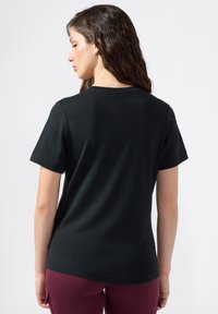 Camiseta de algodón negra con mangas cortas y cuello redondo. Textura suave, diseño ajustado y sin patrones o herrajes visibles.