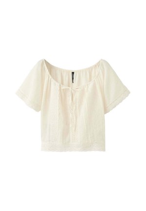 Blouse courte écrue avec manches courtes, bordure en dentelle sur les manches et l’ourlet, panneaux en dentelle à l’avant, et petit lien à nouer à l’avant du col.