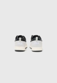 Sorte og grå sneakers med overdel i ruskinn og mesh, en hvit logo på hælen, og en teksturert gummisåle.