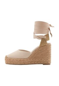 Sandale compensée en toile beige avec une semelle en jute texturée, dotée d'une bride autour de la cheville et d'une légère pointe.