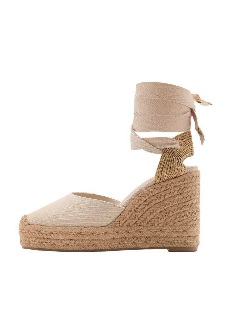 Sandale compensée en toile beige avec une semelle en jute texturée, dotée d'une bride autour de la cheville et d'une légère pointe.