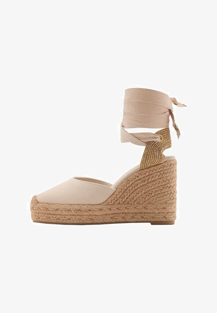 Sandale compensée en toile beige avec une semelle en jute texturée, dotée d'une bride autour de la cheville et d'une légère pointe.