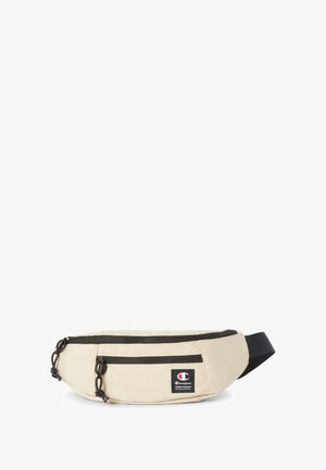 Riñonera de tela beige con dos bolsillos con cremallera, cremalleras y detalles negros, que cuenta con un pequeño parche de logo en la parte frontal. Correa ajustable.
