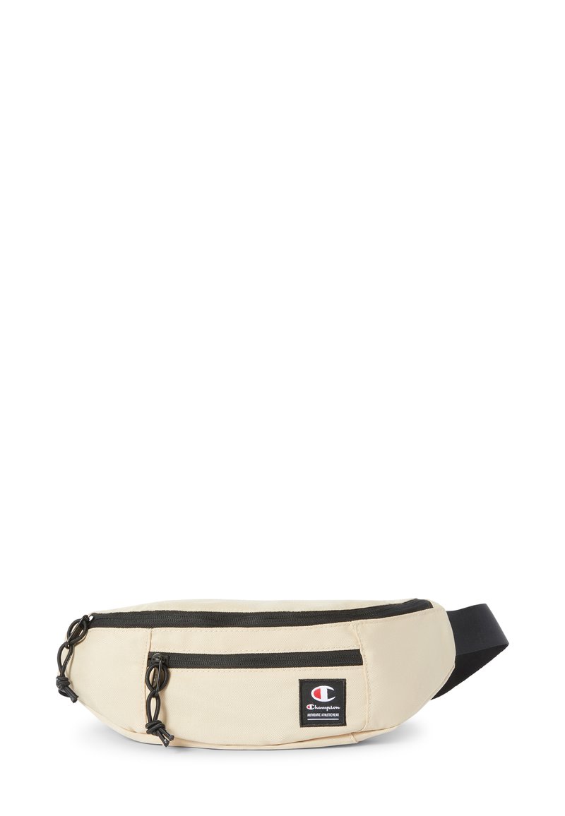 Riñonera de tela beige con dos bolsillos con cremallera, cremalleras y detalles negros, que cuenta con un pequeño parche de logo en la parte frontal. Correa ajustable.