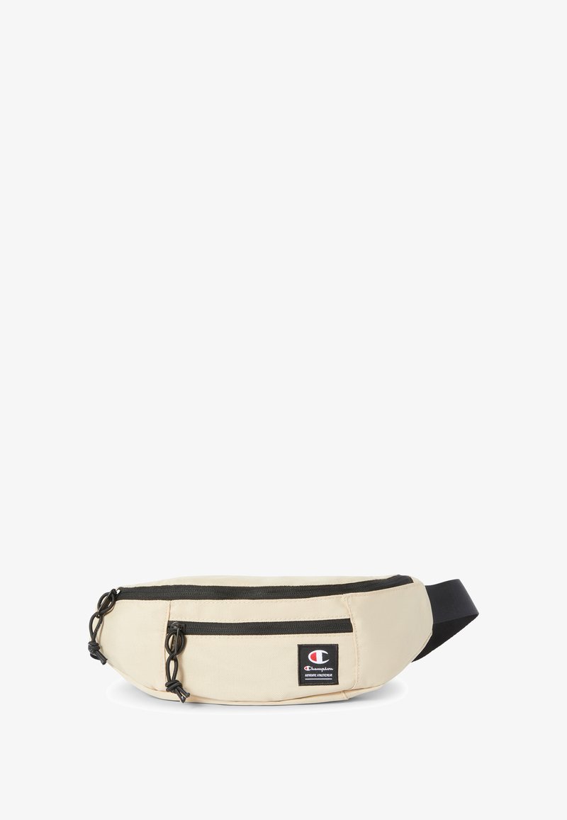 Riñonera de tela beige con dos bolsillos con cremallera, cremalleras y detalles negros, que cuenta con un pequeño parche de logo en la parte frontal. Correa ajustable.