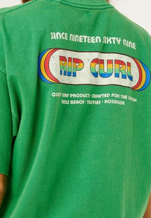 Chemise verte avec le texte multicolore "RIP CURL", "Depuis mille neuf cent soixante-neuf", et les spots de surf Bells Beach, Trestles, Hossegor.