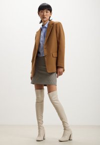 Blazer marrone, camicia azzurro chiaro, gonna mini houndstooth, stivali alti beige con tacco a blocco, texture liscia, outfit a strati.