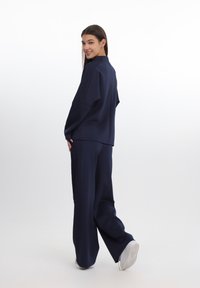 Uniform sportiv albastru marin, realizat dintr-un material texturat. Prezintă mâneci largi și modele complicate pe lateralele bluzei și pantalonilor.
