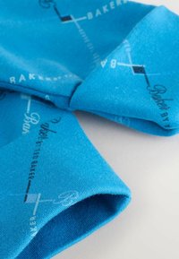Blauer Stoff mit bedrucktem Text und grafischen Elementen, der eine weiche Textur und ein gefaltetes Design aufweist. Das Muster hat ein Bäckerei-Thema.