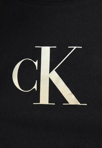 Melnas kokvilnas krekls ar lieliem baltiem burtiem "cK", kas uzdrukāti uz priekšpuses. Audums izskatās gluds ar mīkstu tekstūru.