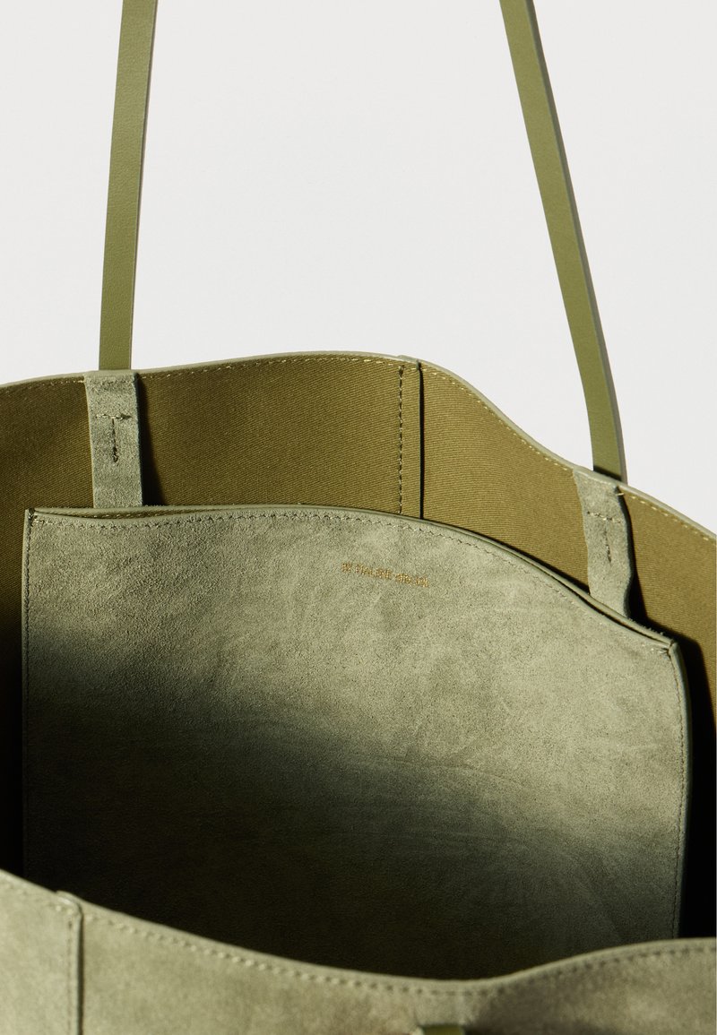 Sac fourre-tout vert avec un extérieur lisse et un intérieur doux, semblable à du daim. Doté de longues anses plates et d'un design minimaliste sans quincaillerie.