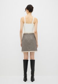 Débardeur blanc, mini-jupe à carreaux marron avec des accents argentés et bottes en cuir noires jusqu'au genou. Tissu lisse avec une coupe structurée.