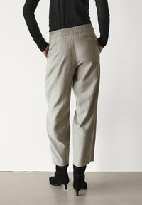 Pantalon gris clair à jambes larges avec une finition texturée et une taille élastique, assorti à des bottines noires pointues.