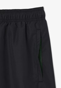 Pantaloni corti blu navy con una fascia elastica in vita, tasche laterali con interno verde a contrasto e una trama di tessuto liscia e leggera.