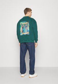 Groene sweatshirt met een graphic print op de achterkant met kleurrijke abstracte kunst. Gekocht met blauwe denim broeken en witte sneakers.