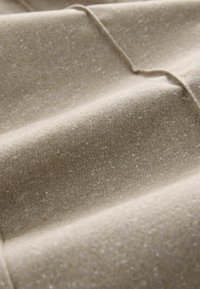 Beige szövet texturált felülettel, amelyen lágy hullámok és finom csillogás található, kiemelve a finom, csillagporra emlékeztető részecskéket.