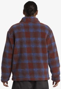Veste en polaire à carreaux marron et bleu, avec une finition douce et texturée et un col, dotée de manches longues et d'une coupe décontractée.